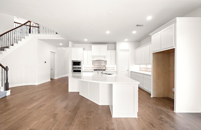 kitchen with white cabinets, appliances with stainless steel finishes, wood-type flooring, and a center island with sink