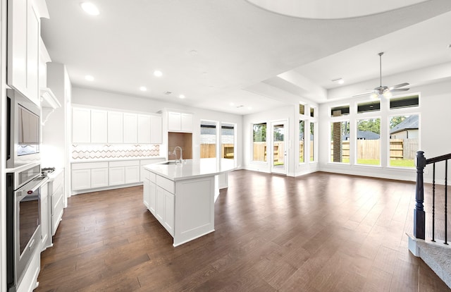 kitchen with sink, backsplash, oven, a kitchen island with sink, and white cabinets