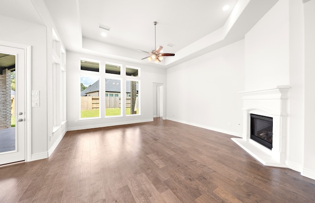 unfurnished living room featuring ceiling fan, a tray ceiling, a large fireplace, and dark hardwood / wood-style floors