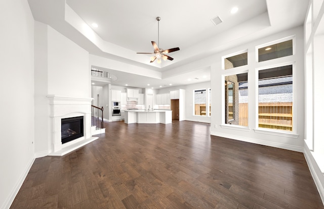 unfurnished living room with dark wood-type flooring, ceiling fan, and a raised ceiling