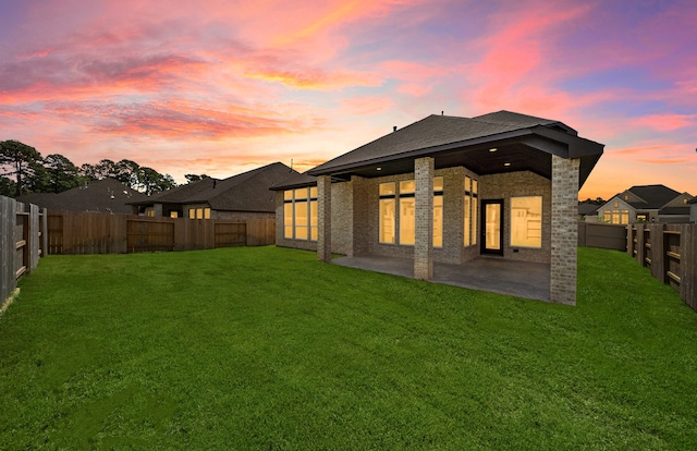 back house at dusk featuring a yard and a patio area