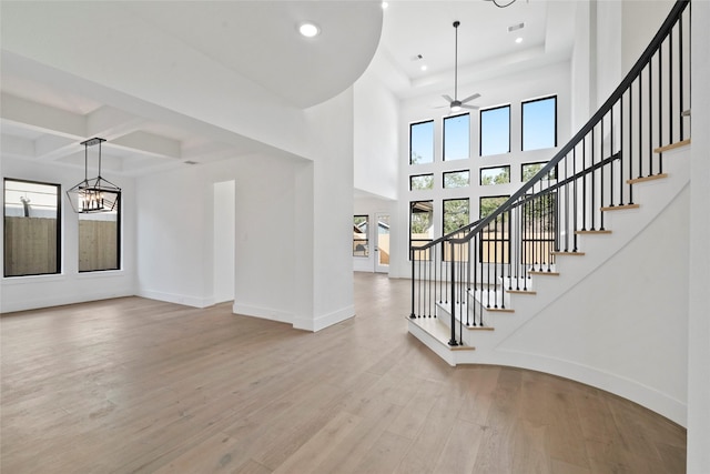 interior space featuring coffered ceiling, ceiling fan with notable chandelier, beamed ceiling, and light hardwood / wood-style flooring