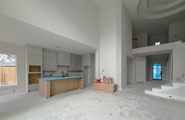 kitchen featuring a high ceiling, open floor plan, a sink, an island with sink, and baseboards