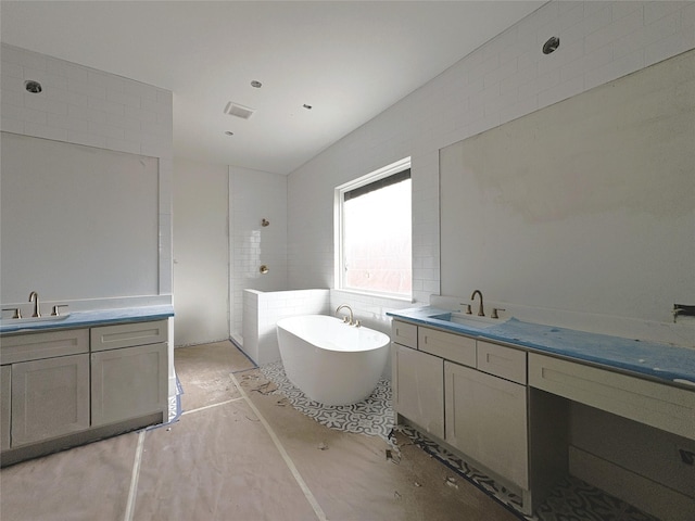 full bath with a freestanding bath, tiled shower, two vanities, and a sink