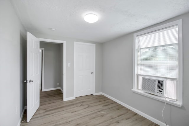 unfurnished bedroom featuring light hardwood / wood-style floors, cooling unit, and a textured ceiling