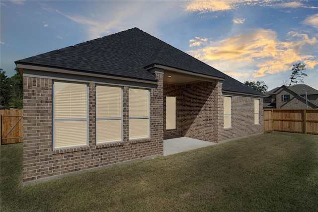 back house at dusk featuring a lawn and a patio area