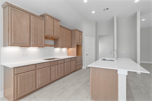 kitchen with light wood-type flooring, backsplash, a center island with sink, and sink