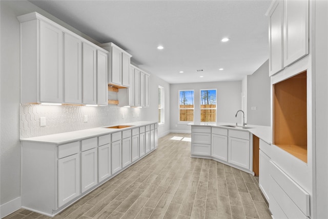 kitchen with light hardwood / wood-style floors, white cabinetry, sink, stovetop, and decorative backsplash