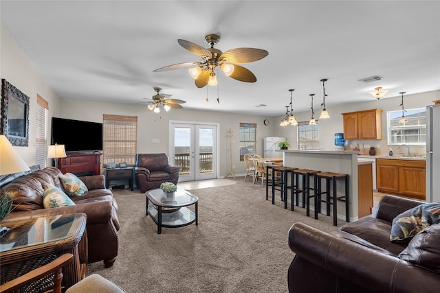 carpeted living room featuring ceiling fan, sink, a healthy amount of sunlight, and french doors