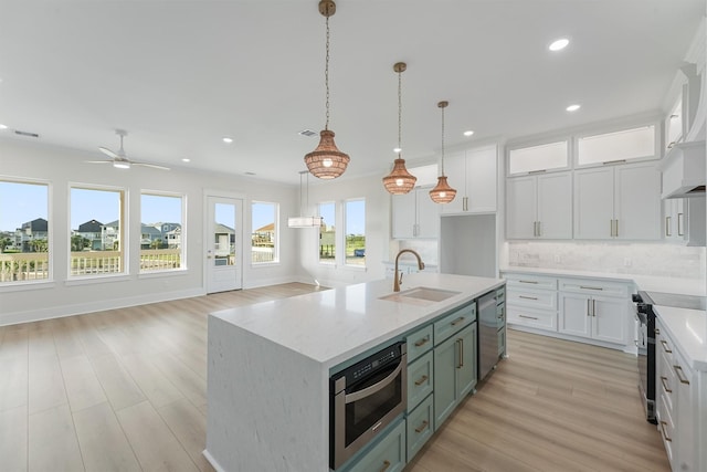 kitchen featuring light wood finished floors, stainless steel appliances, decorative backsplash, white cabinets, and a sink