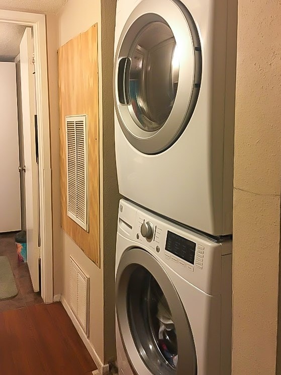 clothes washing area with stacked washing maching and dryer, dark wood-type flooring, and a textured ceiling