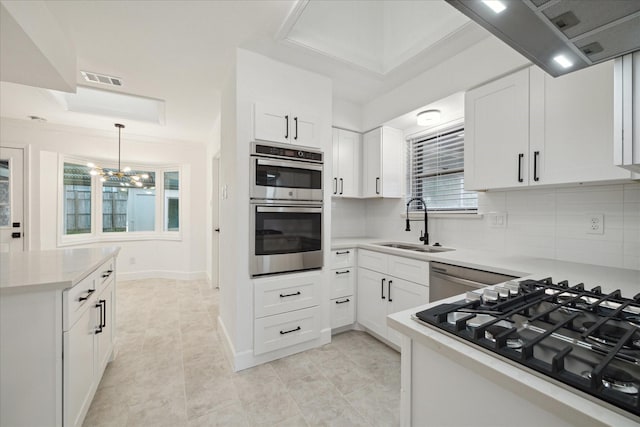 kitchen with stainless steel appliances, a notable chandelier, sink, white cabinetry, and backsplash