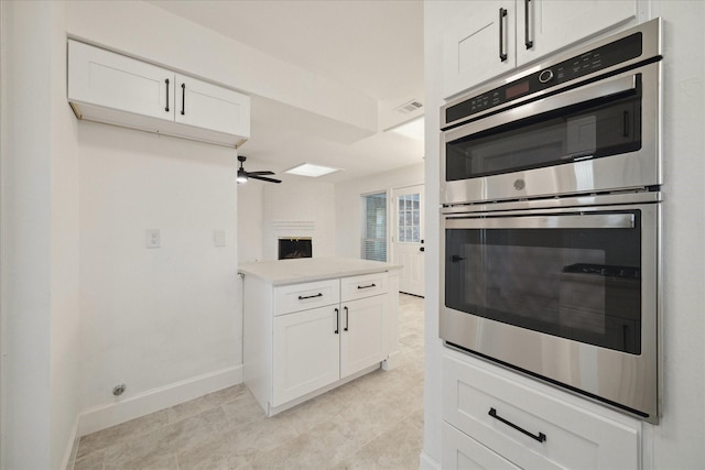 kitchen with double oven, white cabinets, a large fireplace, and ceiling fan