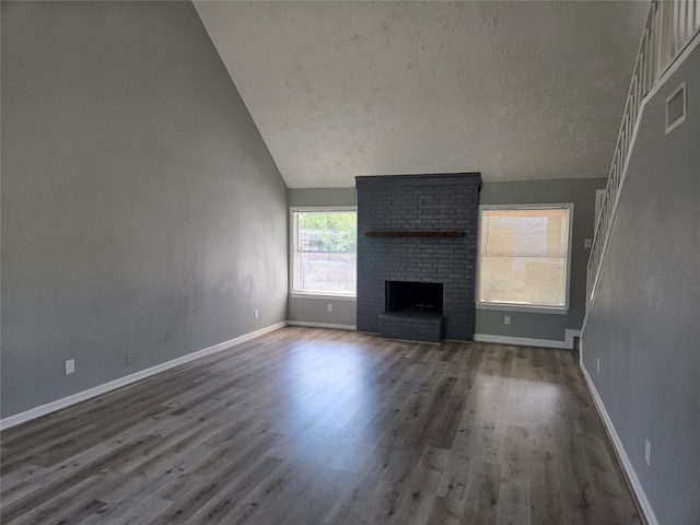 unfurnished living room featuring wood-type flooring, lofted ceiling, a textured ceiling, and a brick fireplace