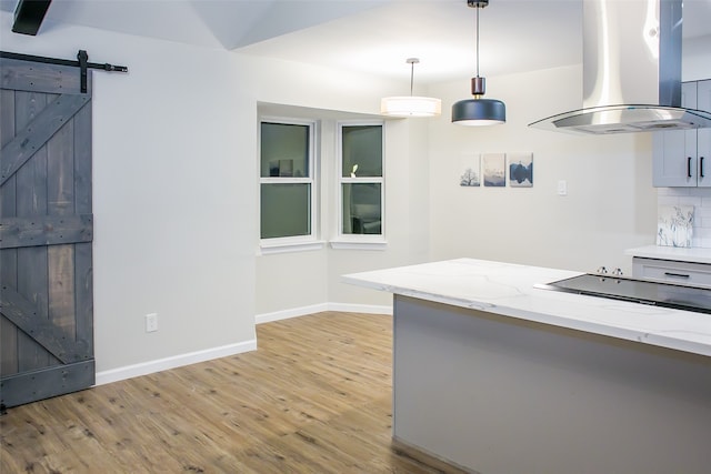 kitchen with island exhaust hood, light stone counters, decorative light fixtures, a barn door, and decorative backsplash