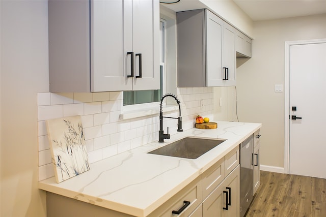 kitchen featuring tasteful backsplash, light stone counters, sink, dishwasher, and light hardwood / wood-style flooring