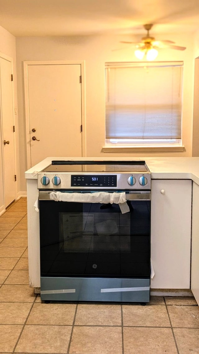 interior details featuring light tile patterned flooring, white cabinetry, ceiling fan, and electric range