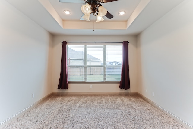 carpeted spare room with ceiling fan and a tray ceiling