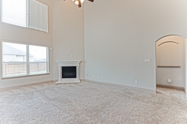 unfurnished living room featuring light carpet, ceiling fan, and a towering ceiling