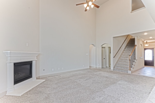 unfurnished living room with light colored carpet, ceiling fan, and a high ceiling