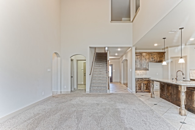 unfurnished living room featuring sink, light colored carpet, ornamental molding, and a towering ceiling