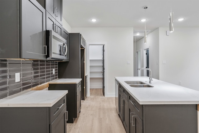 kitchen with decorative backsplash, stainless steel appliances, sink, light hardwood / wood-style flooring, and hanging light fixtures