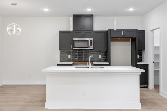 kitchen with decorative backsplash, a kitchen island with sink, sink, light hardwood / wood-style floors, and hanging light fixtures