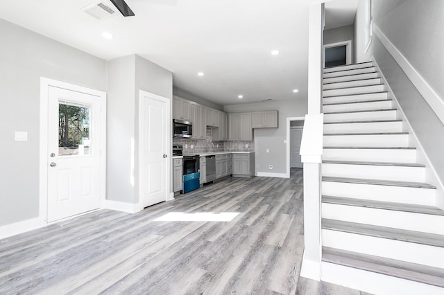 kitchen featuring gray cabinetry, light hardwood / wood-style flooring, appliances with stainless steel finishes, and tasteful backsplash