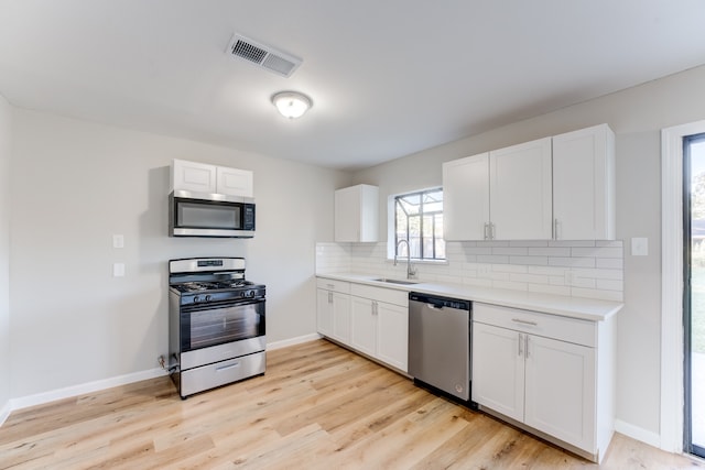 kitchen with decorative backsplash, light hardwood / wood-style flooring, sink, white cabinetry, and appliances with stainless steel finishes