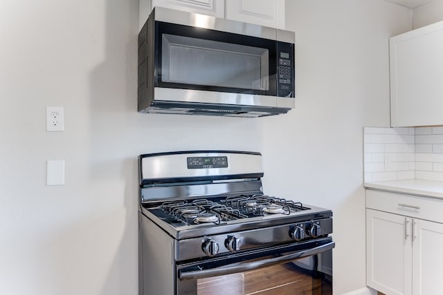 kitchen with stainless steel appliances, wood-type flooring, white cabinetry, and backsplash