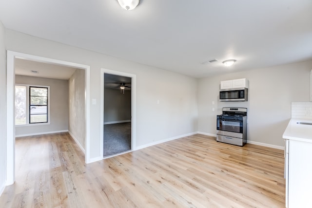 interior space with stainless steel appliances, light hardwood / wood-style floors, ceiling fan, and white cabinets