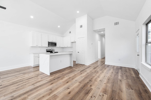 kitchen featuring high vaulted ceiling, light wood-type flooring, white cabinets, and a kitchen island with sink