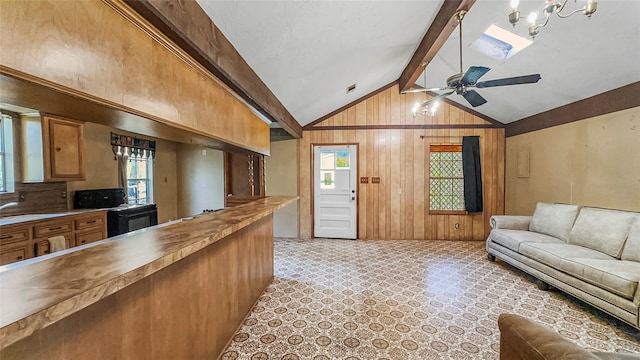 kitchen with ceiling fan, a wealth of natural light, wood walls, and vaulted ceiling with skylight