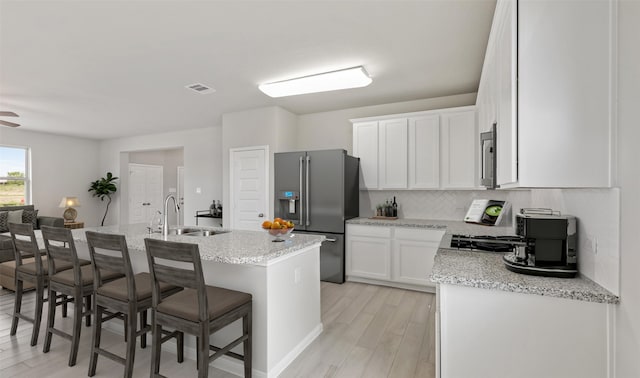 kitchen with white cabinetry, sink, appliances with stainless steel finishes, a kitchen breakfast bar, and an island with sink