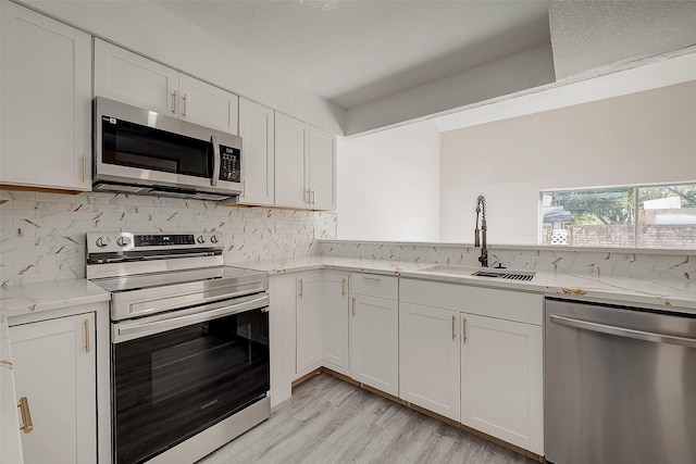 kitchen featuring appliances with stainless steel finishes, light stone counters, white cabinetry, and sink