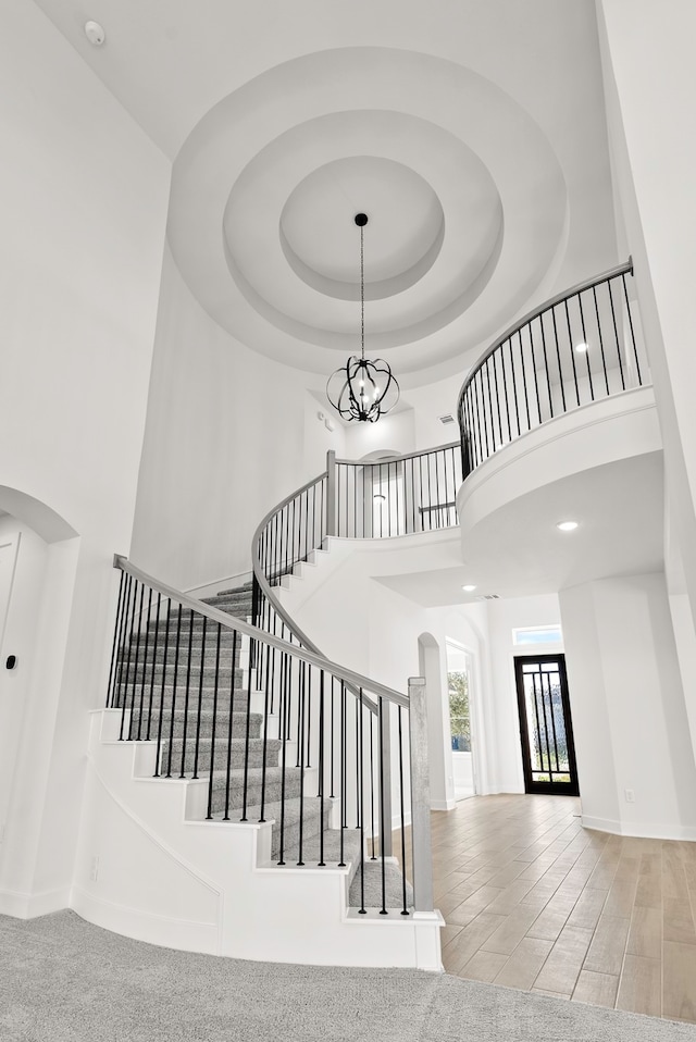 staircase with a chandelier, hardwood / wood-style floors, and a towering ceiling