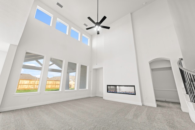 unfurnished living room featuring a high ceiling, light colored carpet, and ceiling fan