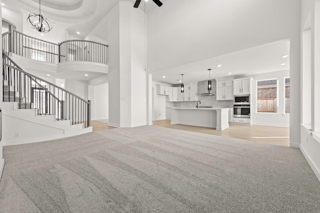 unfurnished living room featuring a high ceiling, sink, light carpet, and ceiling fan with notable chandelier