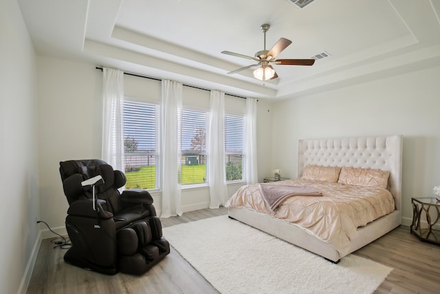 bedroom featuring light wood-type flooring, a raised ceiling, and ceiling fan