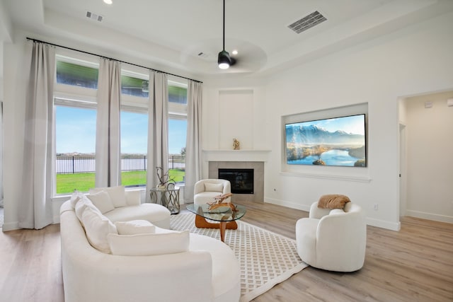 living room with a fireplace, light hardwood / wood-style floors, a raised ceiling, and ceiling fan