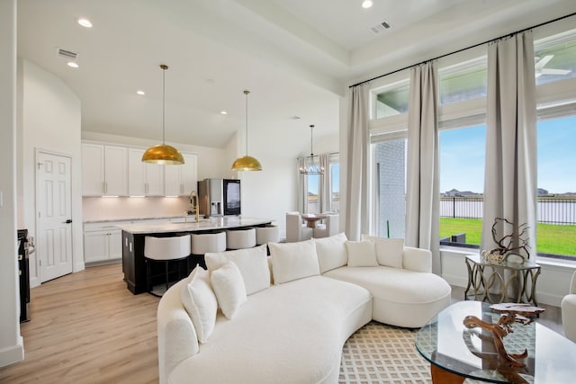 living room featuring vaulted ceiling, sink, and light hardwood / wood-style flooring