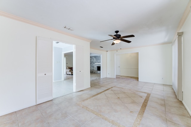 tiled empty room featuring a brick fireplace, ceiling fan, and crown molding