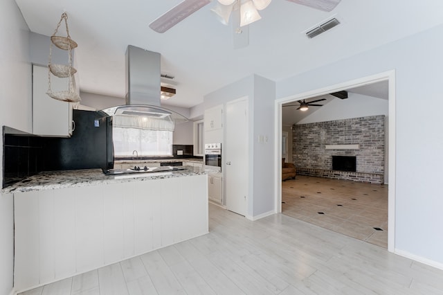 kitchen with white cabinetry, a fireplace, oven, lofted ceiling, and island exhaust hood