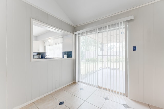 doorway to outside with wooden walls, lofted ceiling, sink, and light tile patterned floors