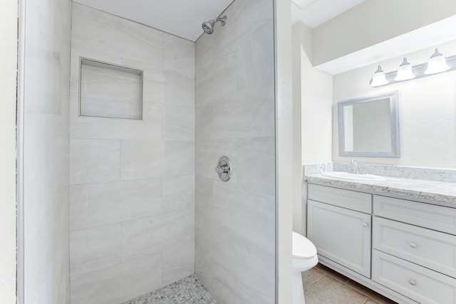 bathroom featuring tile patterned floors, vanity, toilet, and a tile shower