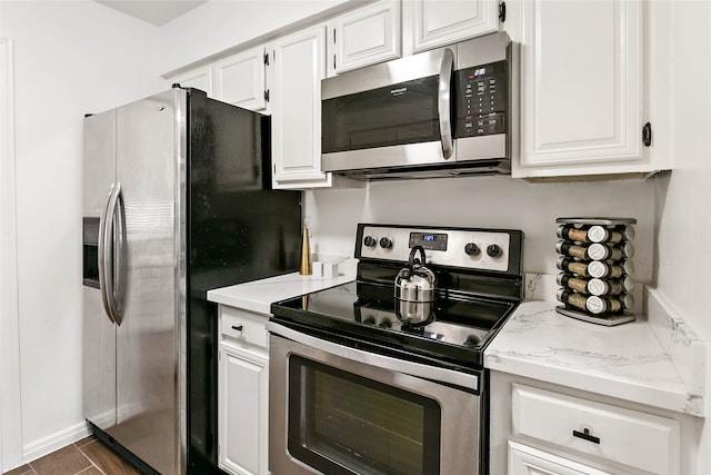 kitchen featuring stainless steel appliances, white cabinets, dark tile patterned floors, and light stone counters