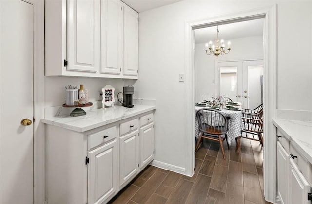 kitchen with white cabinets, dark wood-type flooring, a chandelier, and light stone countertops