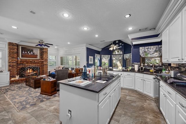 kitchen with white cabinetry, a center island, ceiling fan, a brick fireplace, and crown molding