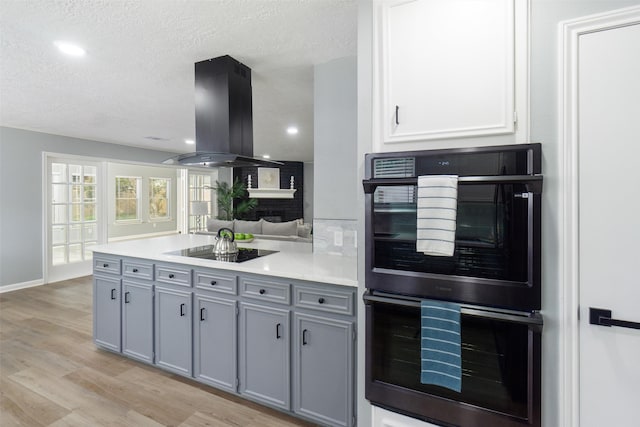 kitchen featuring black appliances, island range hood, gray cabinets, and a textured ceiling