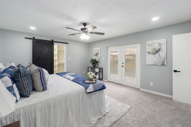 bedroom with access to exterior, a walk in closet, ceiling fan, a barn door, and carpet floors